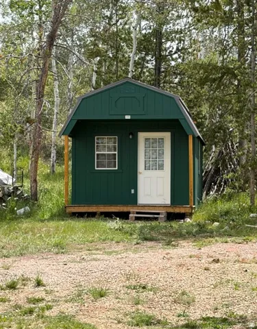 Green gambrel-roofed structure with a white entry door and a single grid-paned window