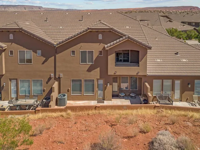 Terraced townhome exterior featuring an upper-level balcony, ground-level patios, and stucco siding