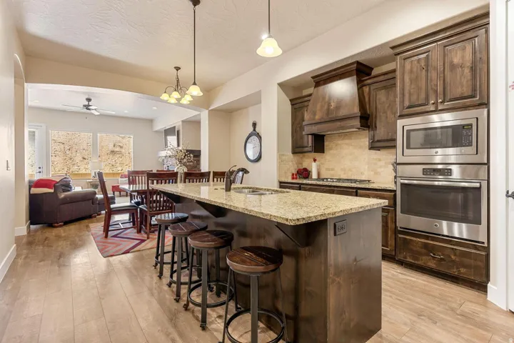 Kitchen featuring a large island with a stone countertop, dark wood-finish cabinetry, stainless steel appliances, a built-in oven and microwave, and wood-finish flooring