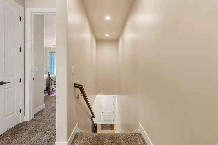 Carpeted stairway with a dark wood-finish handrail, recessed lighting, and light neutral wall paint