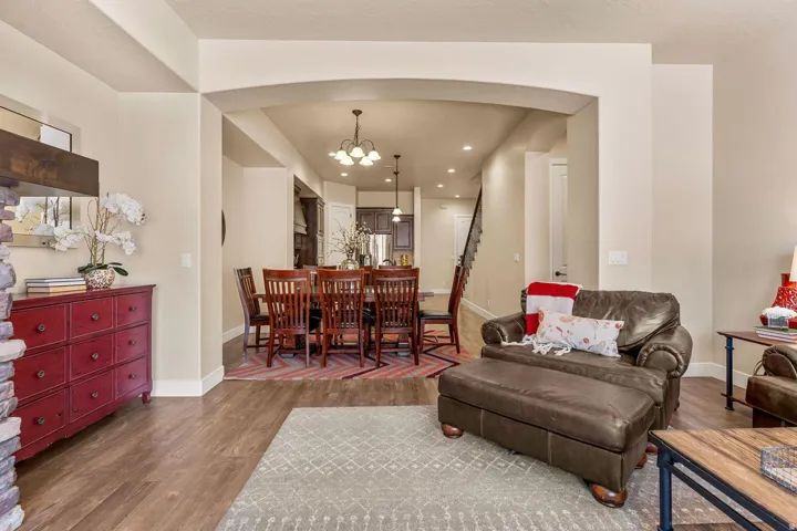 Open-concept living area with wood-finish flooring, arched doorways, a stone-clad fireplace, recessed lighting, and a staircase with dark wood railings