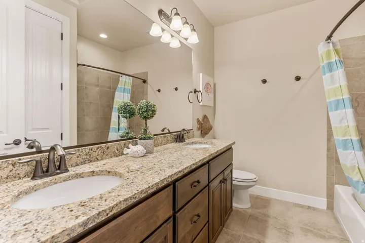 Bathroom featuring a double vanity with granite-style countertops, integrated sinks, dark wood-finish cabinetry, and oil-rubbed bronze fixtures