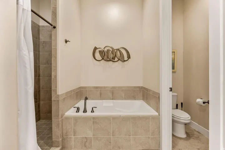 Bathroom featuring a built-in soaking tub with dark-toned fixtures, a tiled surround, and a coordinating tiled shower enclosure