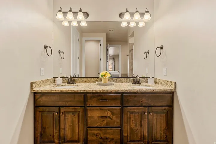 Dual vanity featuring a granite countertop, integrated sinks, and dark wood cabinetry