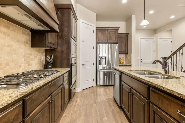 Kitchen featuring dark wood cabinetry, light granite countertops, stainless steel appliances, a tiled backsplash, and wood-finish flooring