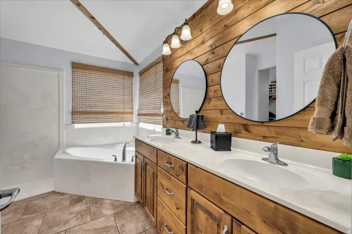 Bathroom featuring a dual vanity with wood cabinetry and white countertops, individual circular mirrors, a built-in soaking tub, and tile flooring