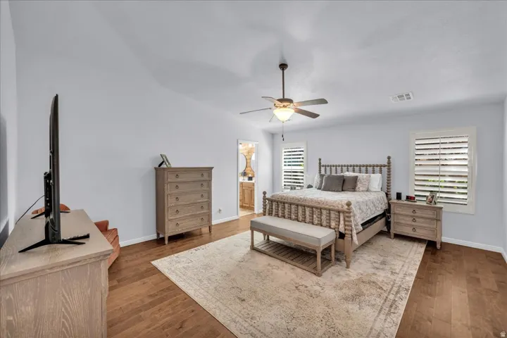 Spacious room featuring wood-finish flooring, vaulted ceiling, and dual window openings with plantation shutters