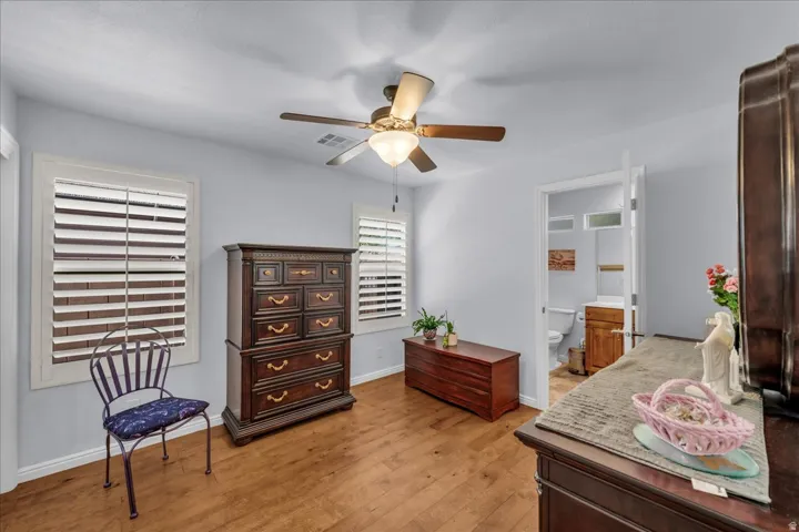 Room featuring wood-finish flooring, two window openings with plantation shutters, and a ceiling fan with light fixture