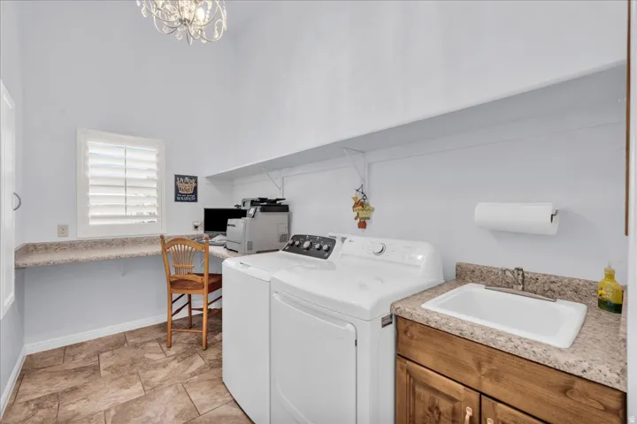 Laundry room featuring tiled flooring, a utility sink with wood-finish cabinetry, a built-in countertop, and white plantation shutters on the window