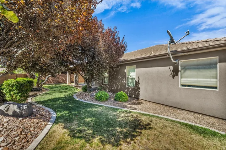 Exterior landscaping featuring mature trees providing natural shade, a manicured lawn, and decorative rock beds with concrete curbing