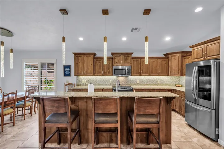 Spacious kitchen featuring an expansive center island, tile flooring, wood cabinetry, stainless steel appliances, and pendant lighting