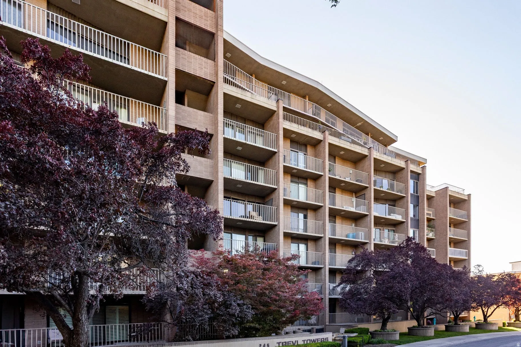 Multi-story residential building featuring a light-toned brick facade with individual balconies