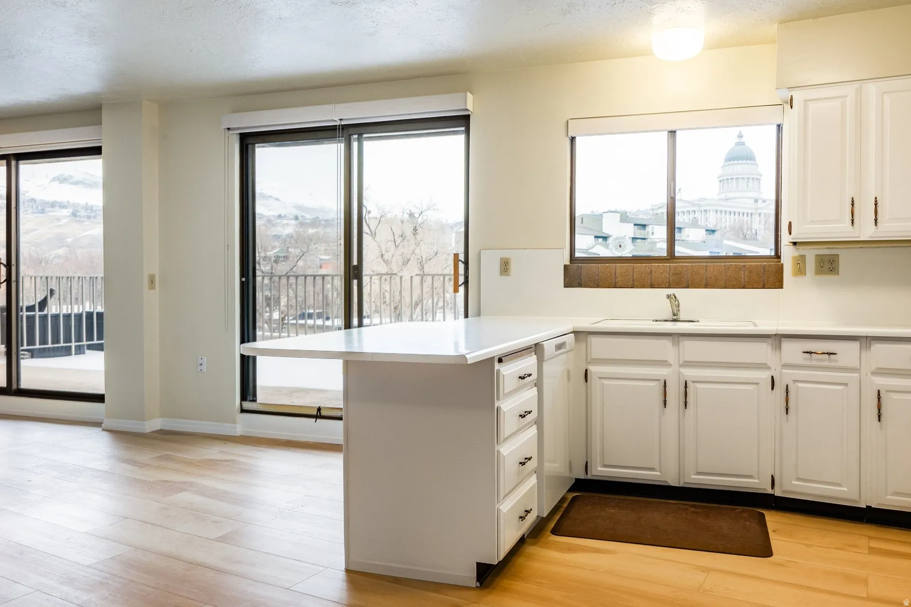 Kitchen area featuring light wood-finish flooring, white cabinetry, and a white countertop with an integrated breakfast bar