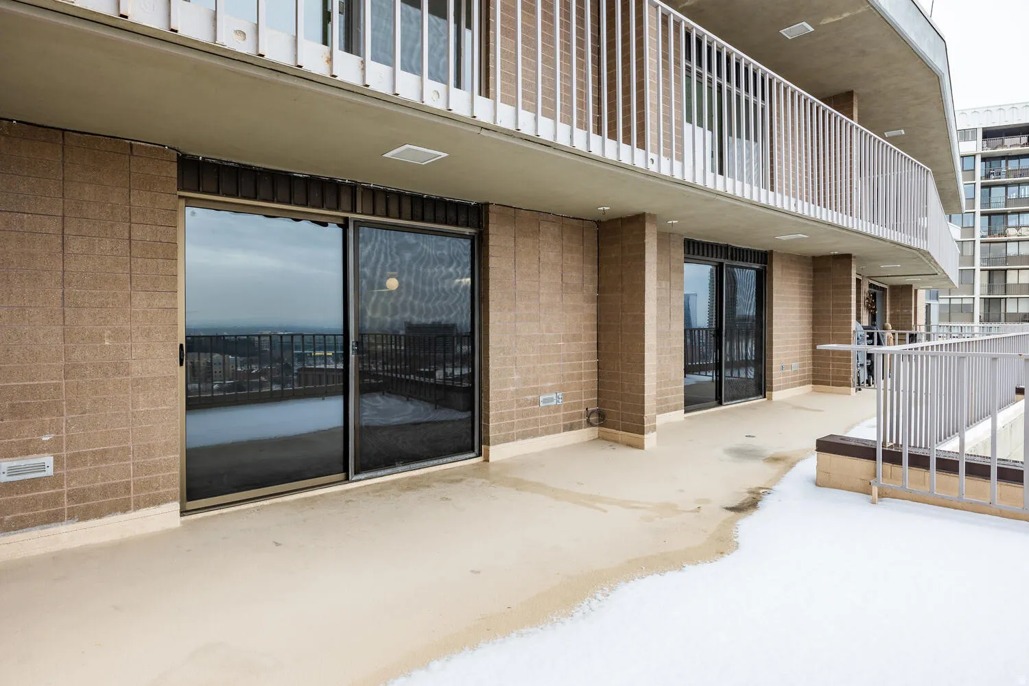 Expansive balcony with concrete flooring, brown brick facade, and sliding glass doors