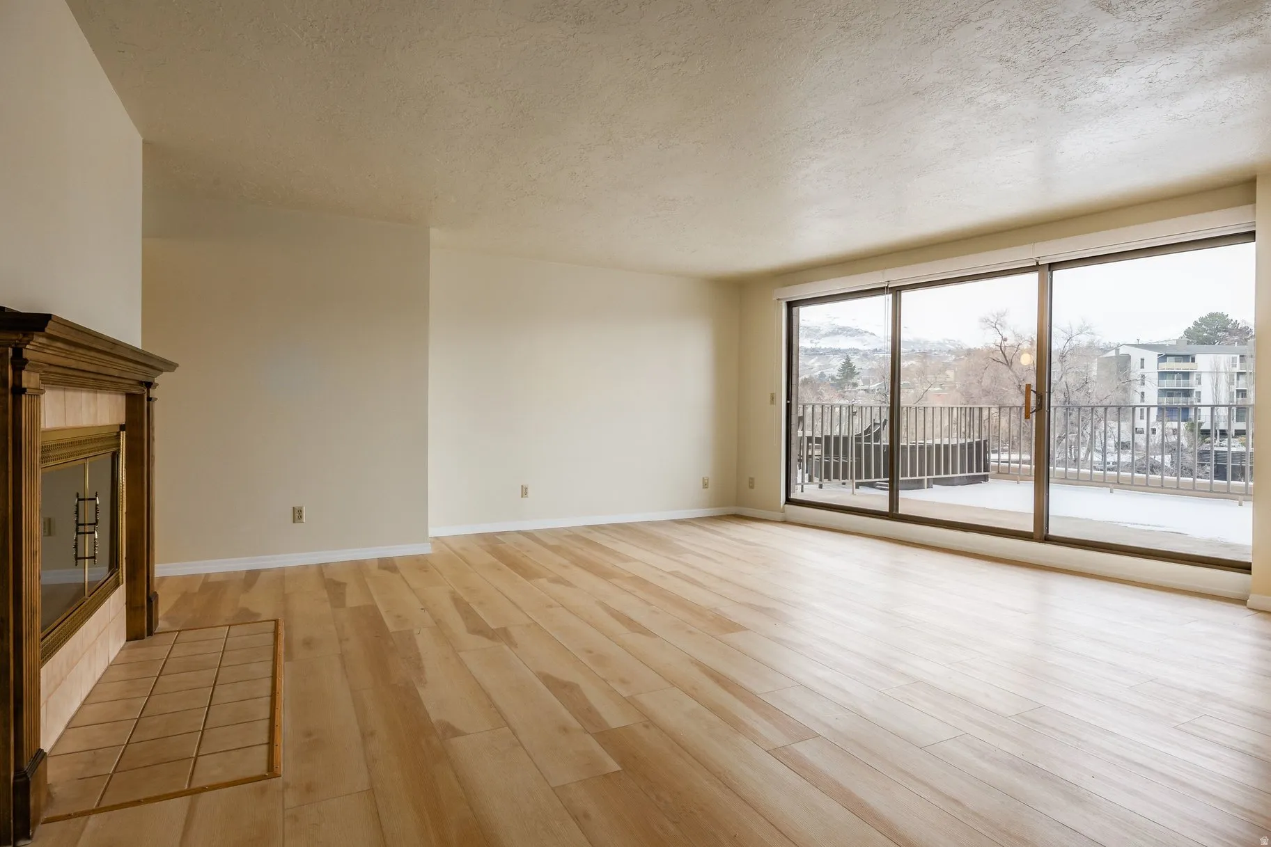 Spacious room featuring wood-finish flooring, a traditional fireplace with a tiled hearth, and a full wall of sliding glass doors leading to a private outdoor balcony