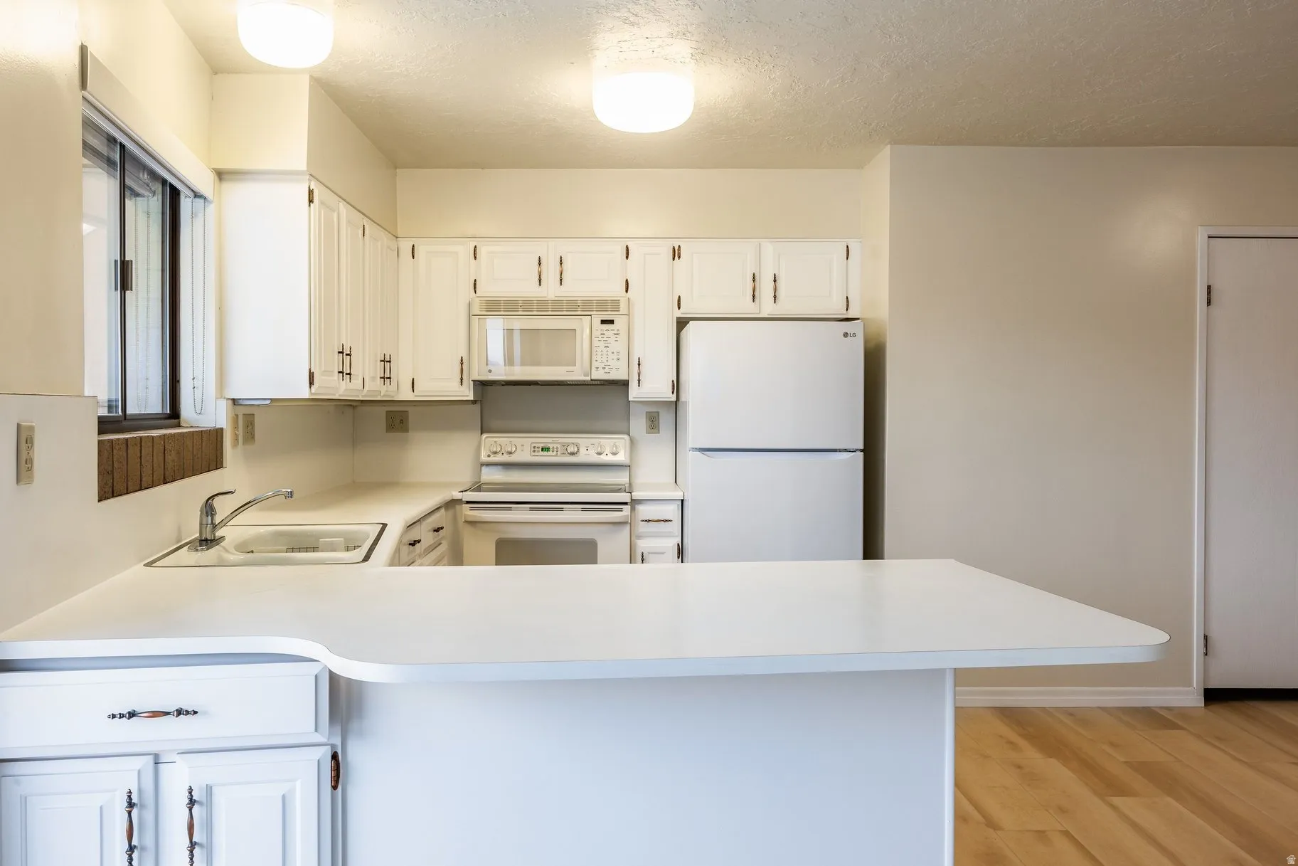 Kitchen featuring white cabinetry and appliances, a double basin sink with chrome faucet, a peninsula countertop, and wood-finish flooring