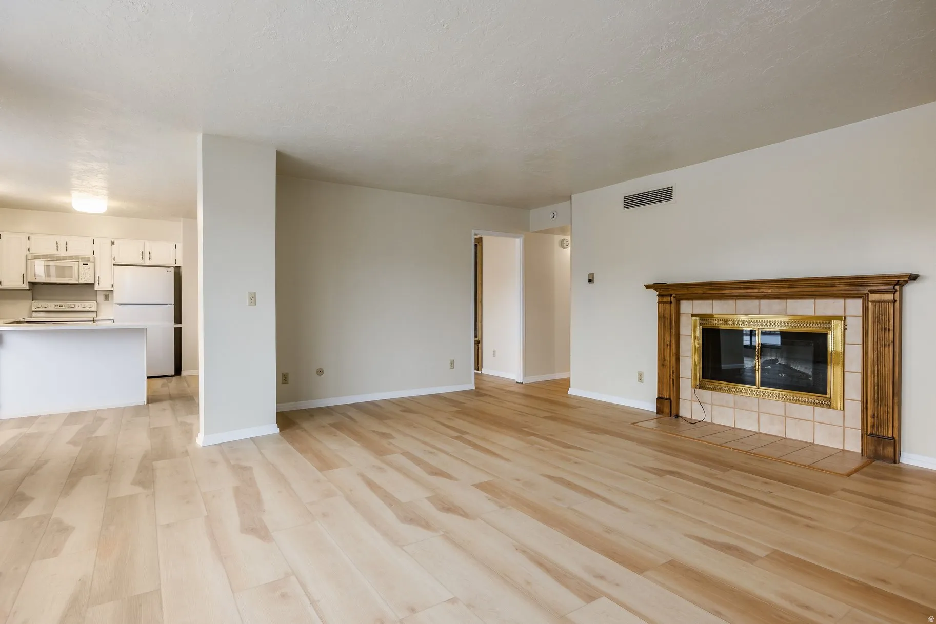 Living area featuring wood-finish flooring, a fireplace with a wood mantle and tile surround, and an adjacent kitchen with white cabinetry and an island