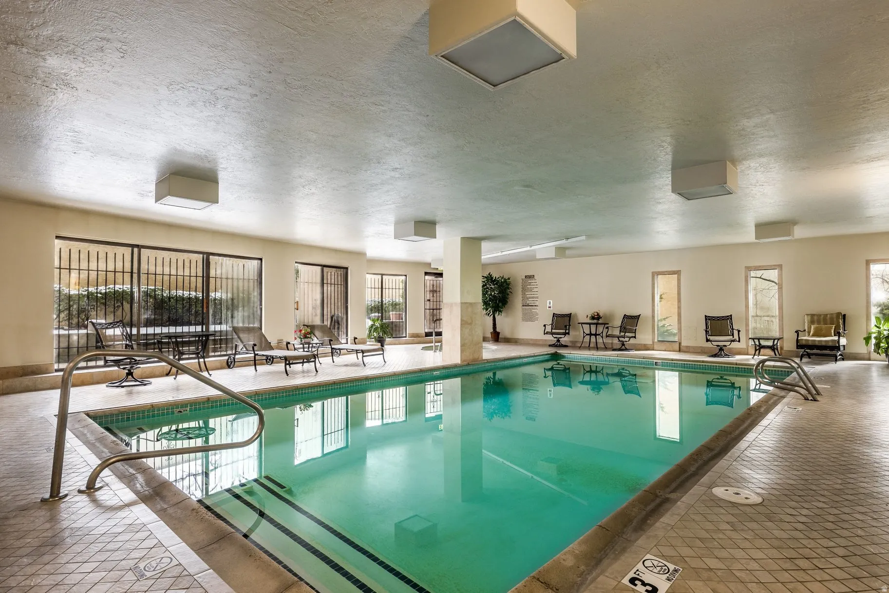 Indoor swimming pool featuring tiled surround and metal handrails
