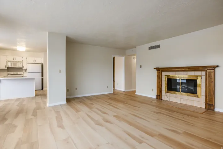 Living area featuring wood-finish flooring, a fireplace with a wood mantle and tile surround, and an adjacent kitchen with white cabinetry and an island