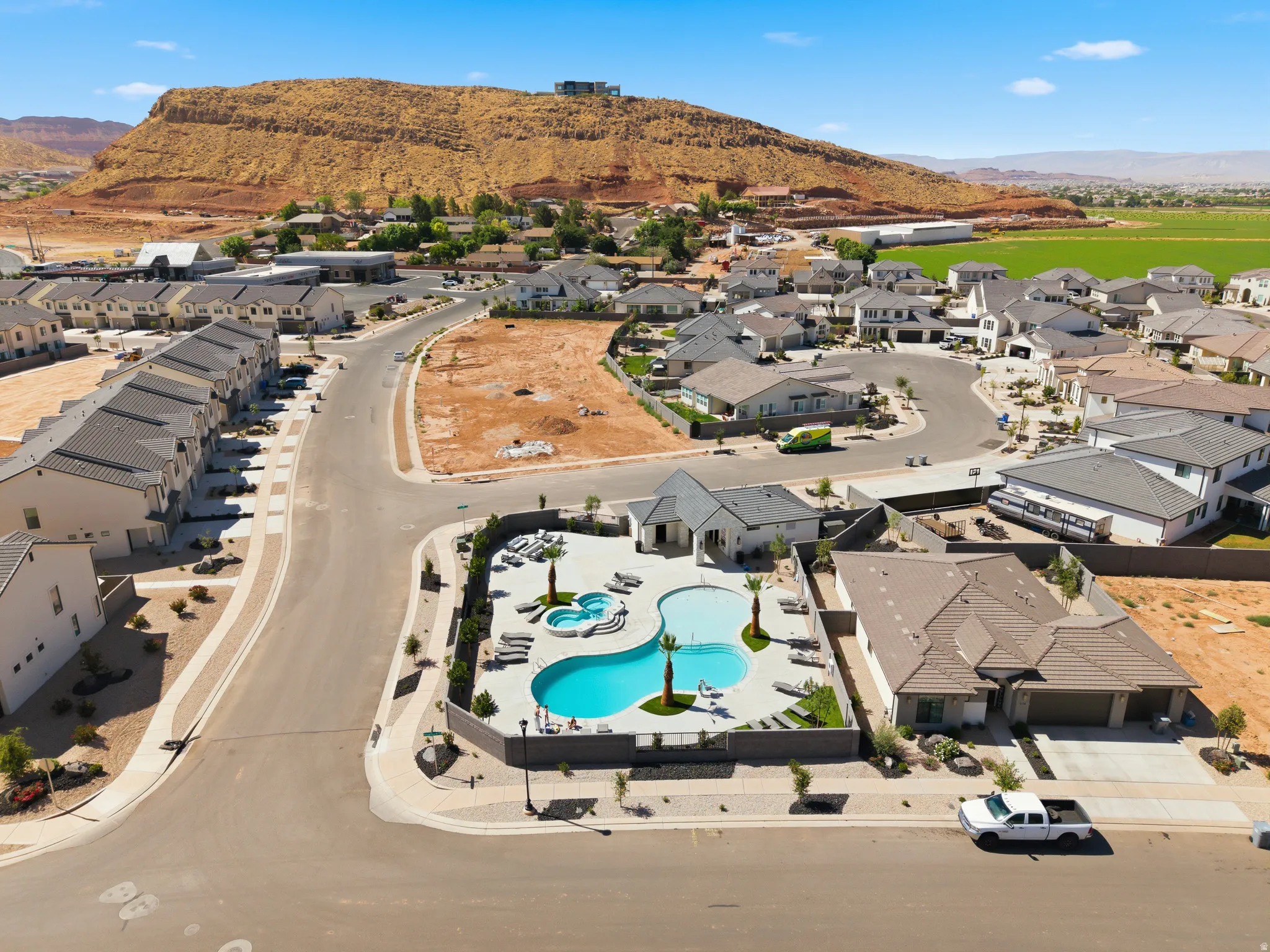 Aerial perspective of a residential community featuring a curvilinear swimming pool with an integrated spa, surrounded by lounge seating and palm trees