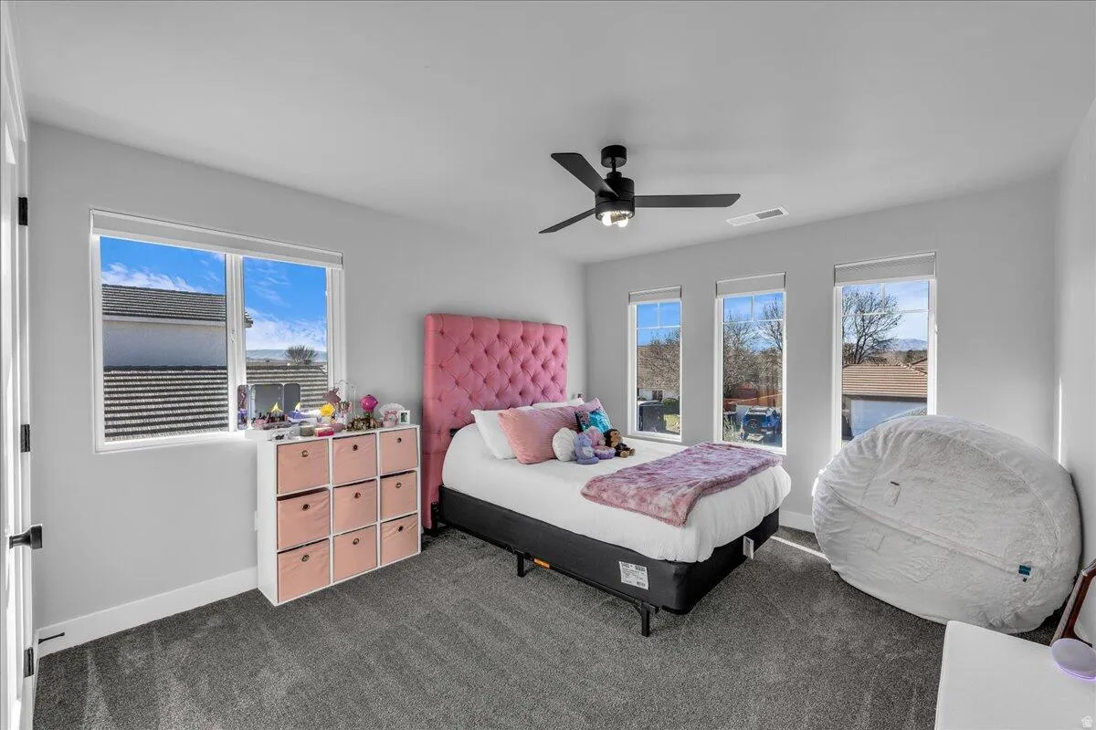 Gray wall paint, gray carpet, multiple windows, and a ceiling fan with integrated lighting