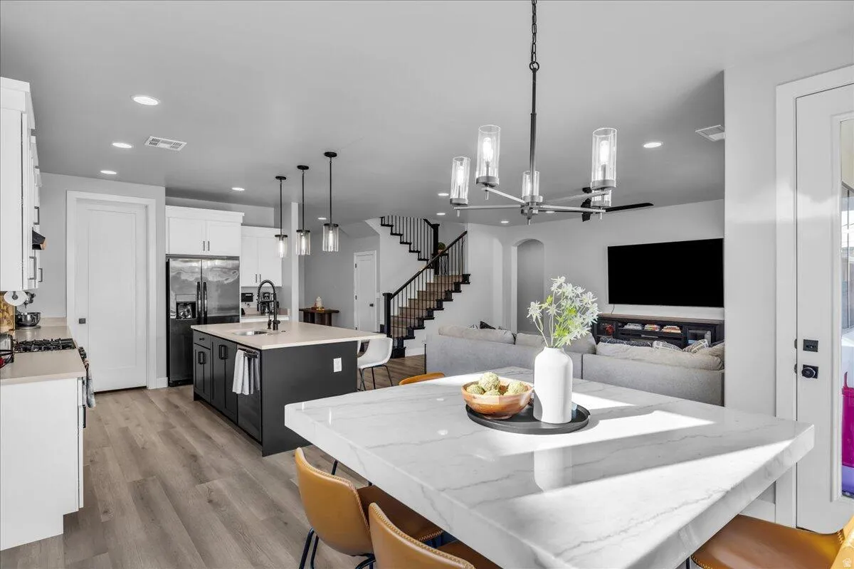 Open-concept living space featuring a kitchen with white cabinetry and a dark island with a light-toned countertop, wood-finish flooring, a contemporary chandelier, and a staircase with dark railings