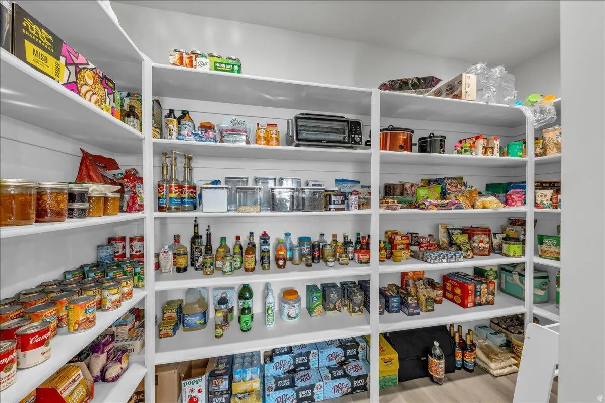 Expansive walk-in pantry featuring multiple levels of white shelving and light wood-finish flooring