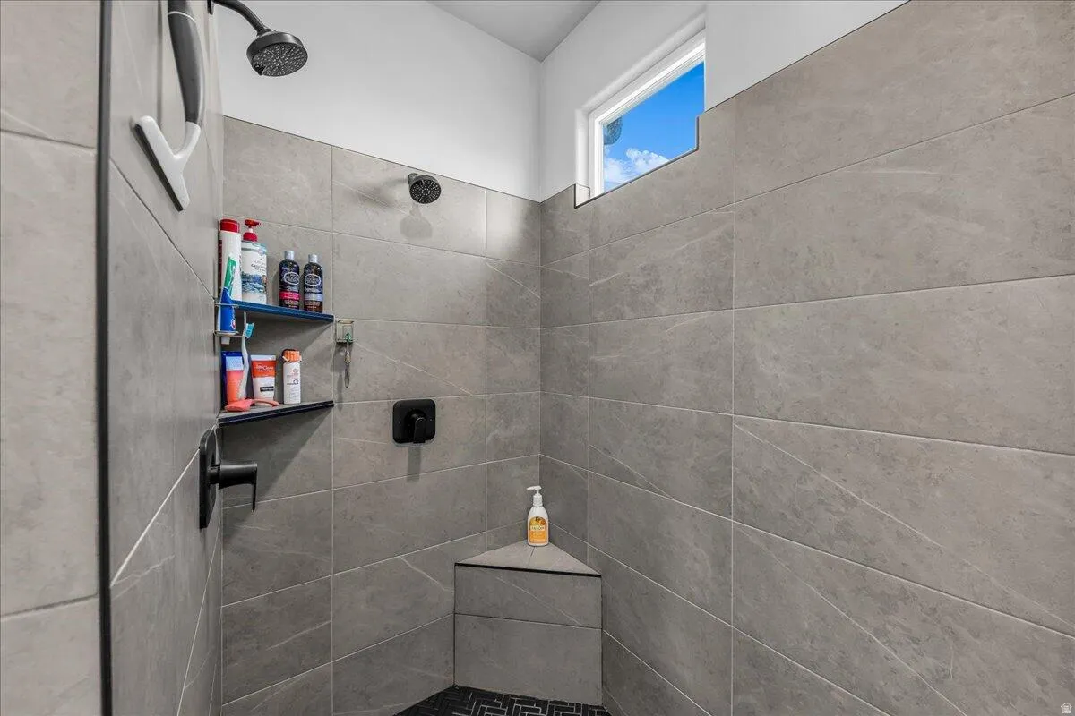 Spacious shower enclosure featuring large format grey tile walls, a built-in corner bench, and a black hexagon tile floor