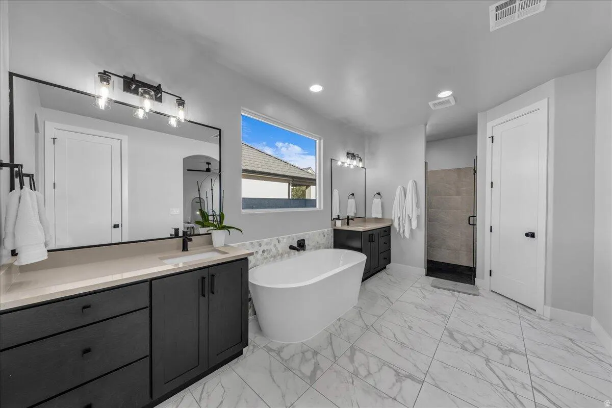 Spacious bathroom featuring a freestanding tub, dual vanities with light countertops, a walk-in shower with tile surround, and large format marble-look floor tiles