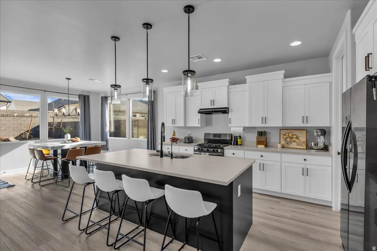 Open-concept kitchen featuring an oversized island, white shaker cabinetry, stainless steel appliances, and light wood-finish flooring