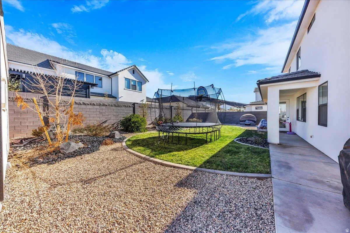 Spacious backyard featuring a manicured lawn, gravel landscaping, a concrete patio, and block perimeter fencing