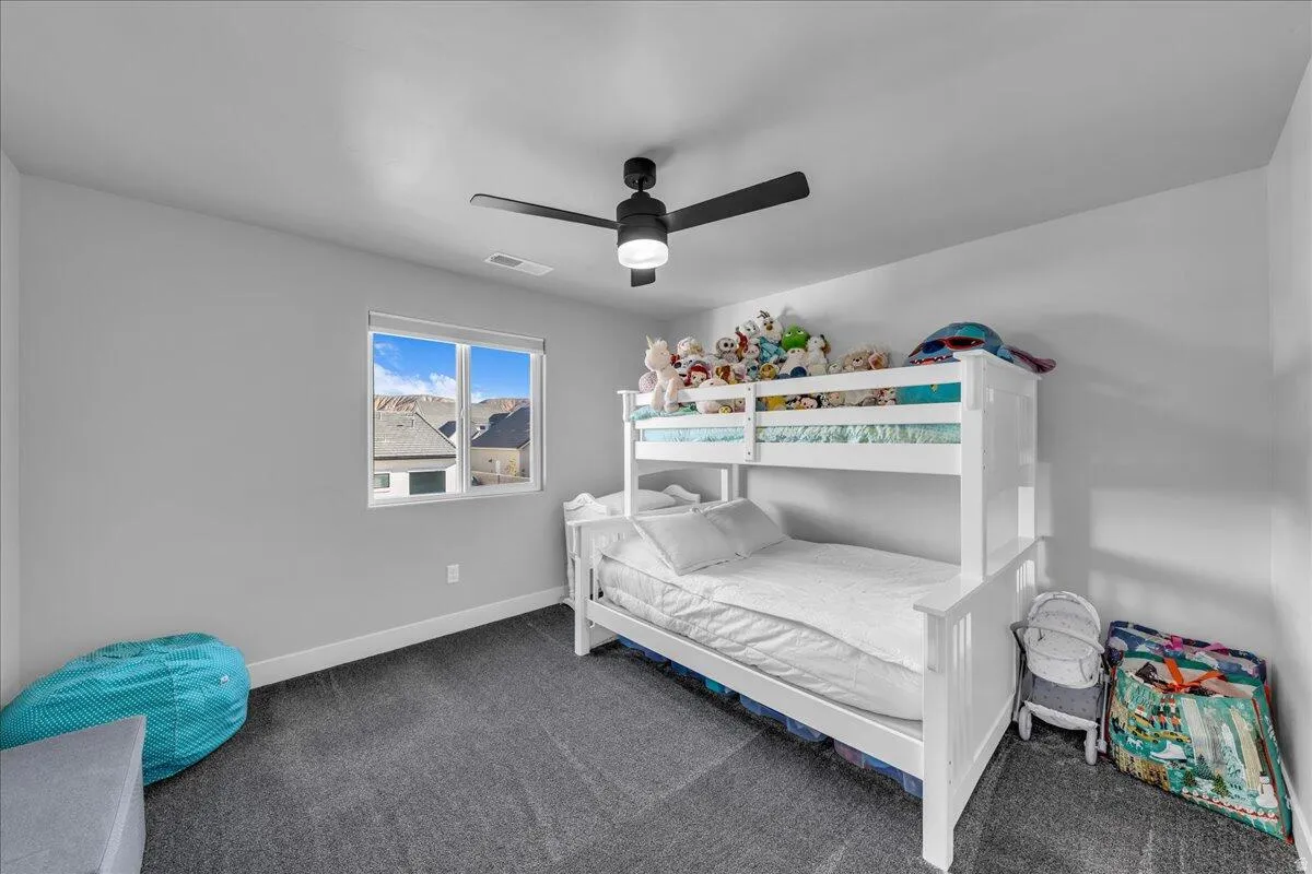 Room featuring a window, dark gray carpeting, light gray walls, and a black ceiling fan with integrated lighting