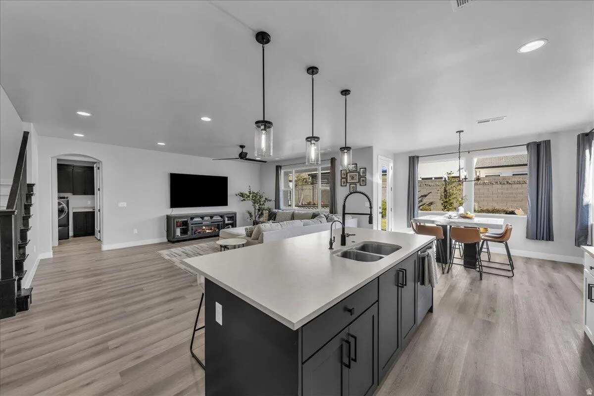 Kitchen island with a light-toned countertop and dark cabinetry featuring a double sink and pendant lighting