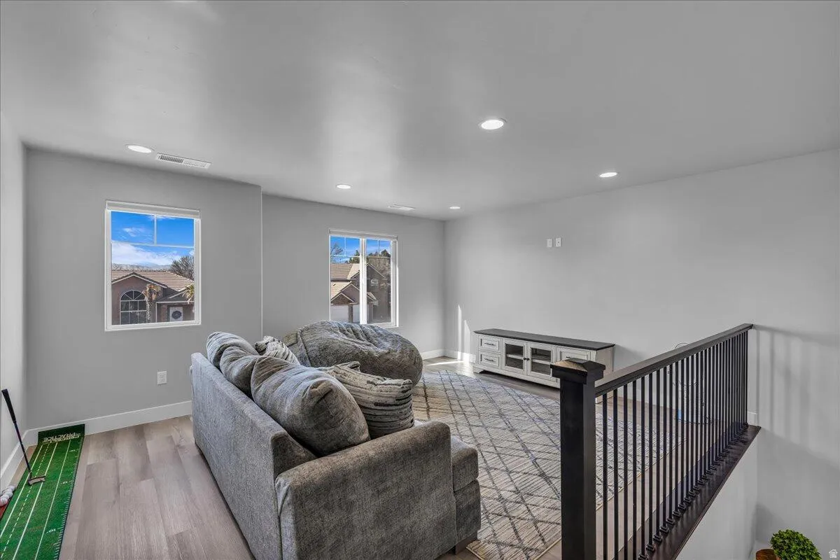 Spacious upper-level room featuring light gray walls, recessed lighting, and wood-finish flooring