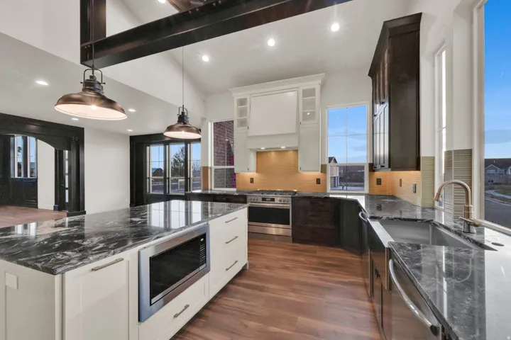 Open-concept kitchen featuring an oversized island with a built-in microwave, wood-finish flooring, two-tone cabinetry, stainless steel appliances, and abundant natural light