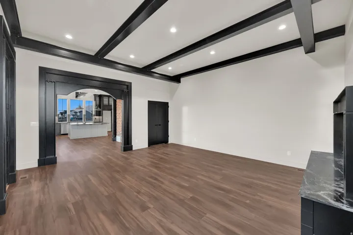 Spacious room featuring wood-finish flooring, a coffered ceiling with recessed lighting, and a decorative archway