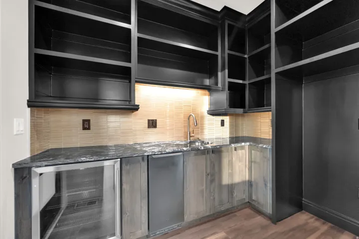 Wet bar featuring dark cabinetry, stone countertops, a tile backsplash, an undermount sink with a gooseneck faucet, and integrated beverage refrigeration