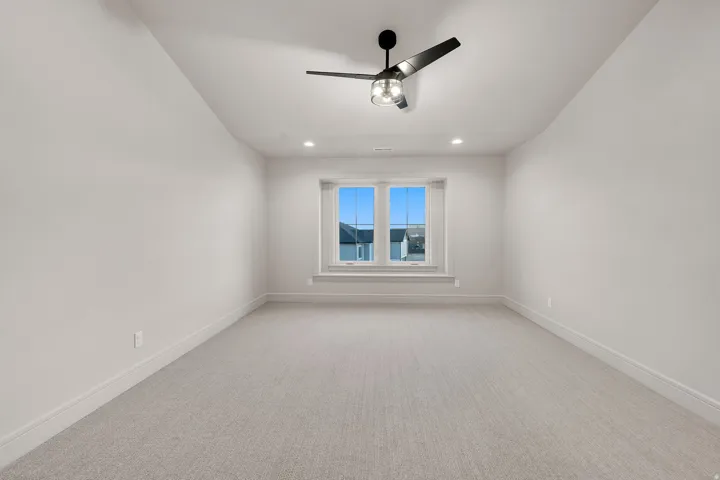 Spacious room featuring light-toned carpeting, a large window, a black ceiling fan, recessed lighting, and crisp white baseboards