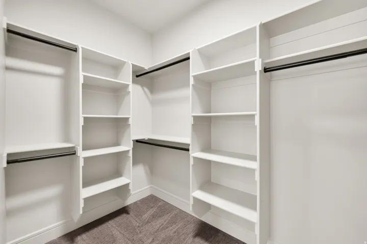 Walk-in closet featuring white built-in shelving, multiple hanging rods, and textured carpet flooring