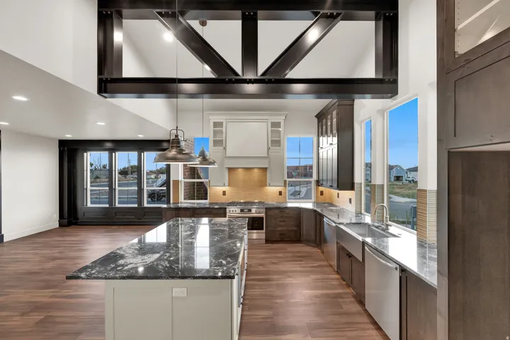 Open-concept kitchen with a large island featuring a polished granite countertop, wood-finish flooring, exposed structural beams, full-height cabinetry, and a stainless steel farmhouse sink
