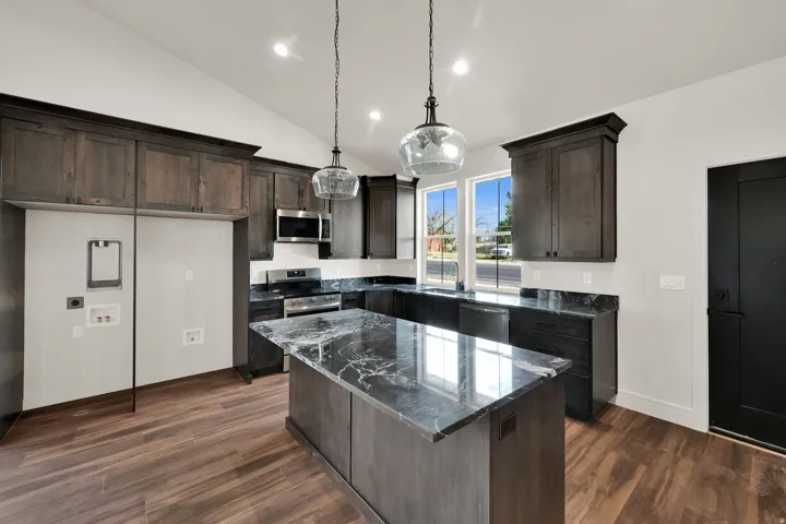 Spacious kitchen featuring an expansive island with a stone countertop, dark wood-finish cabinetry, stainless steel appliances, and wood-finish flooring