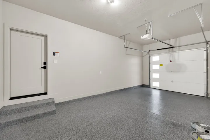 Spacious garage with an epoxy-coated concrete floor, a white paneled overhead door with frosted glass inserts, and an automatic garage door opener