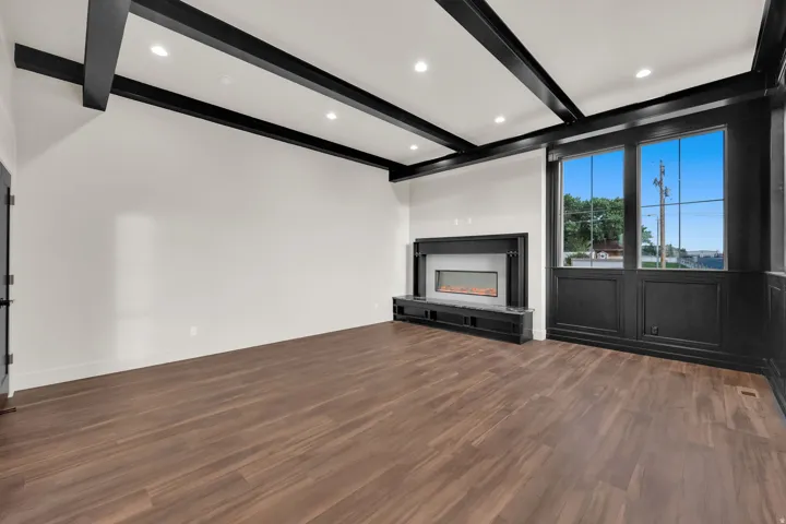 Spacious interior featuring dark wood-finish flooring, a linear fireplace with a stone hearth, recessed lighting, and exposed ceiling beams