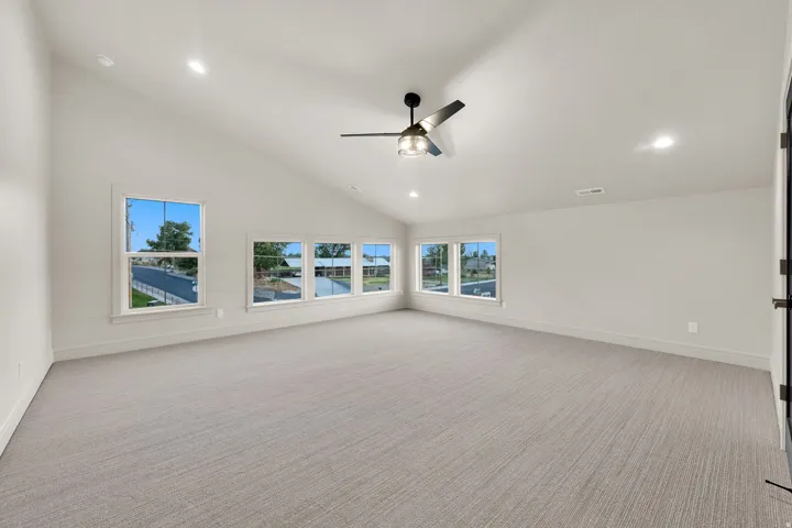 Spacious room featuring vaulted ceilings, recessed lighting, a modern ceiling fan, five windows, and light gray carpeted flooring