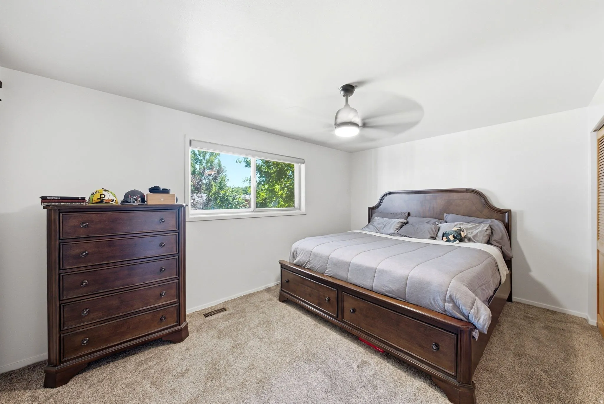 Carpeted room with a ceiling fan, a window, and a louvered closet door