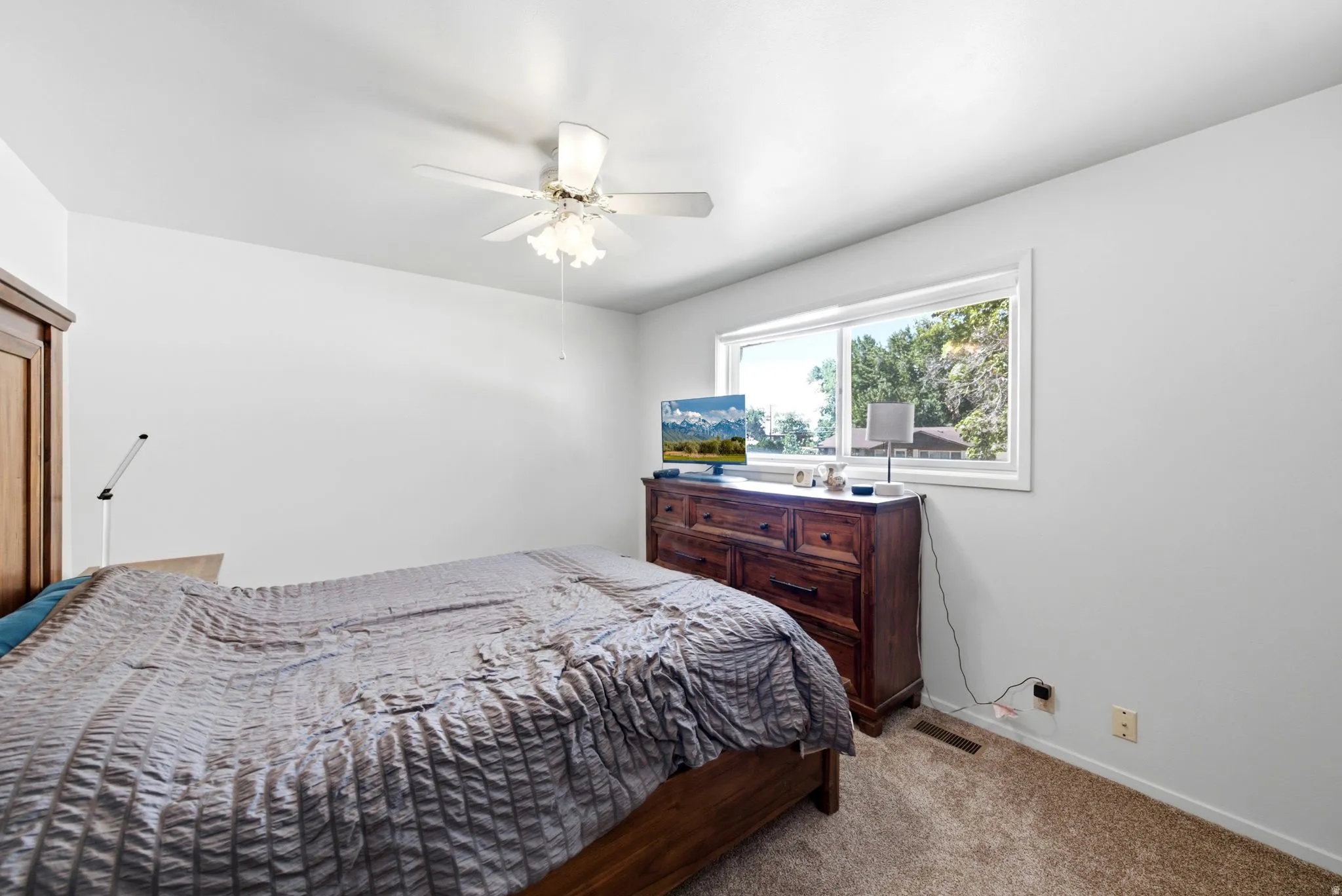 Neutral wall color, carpet flooring, a ceiling fan with light fixture, and a window with white trim