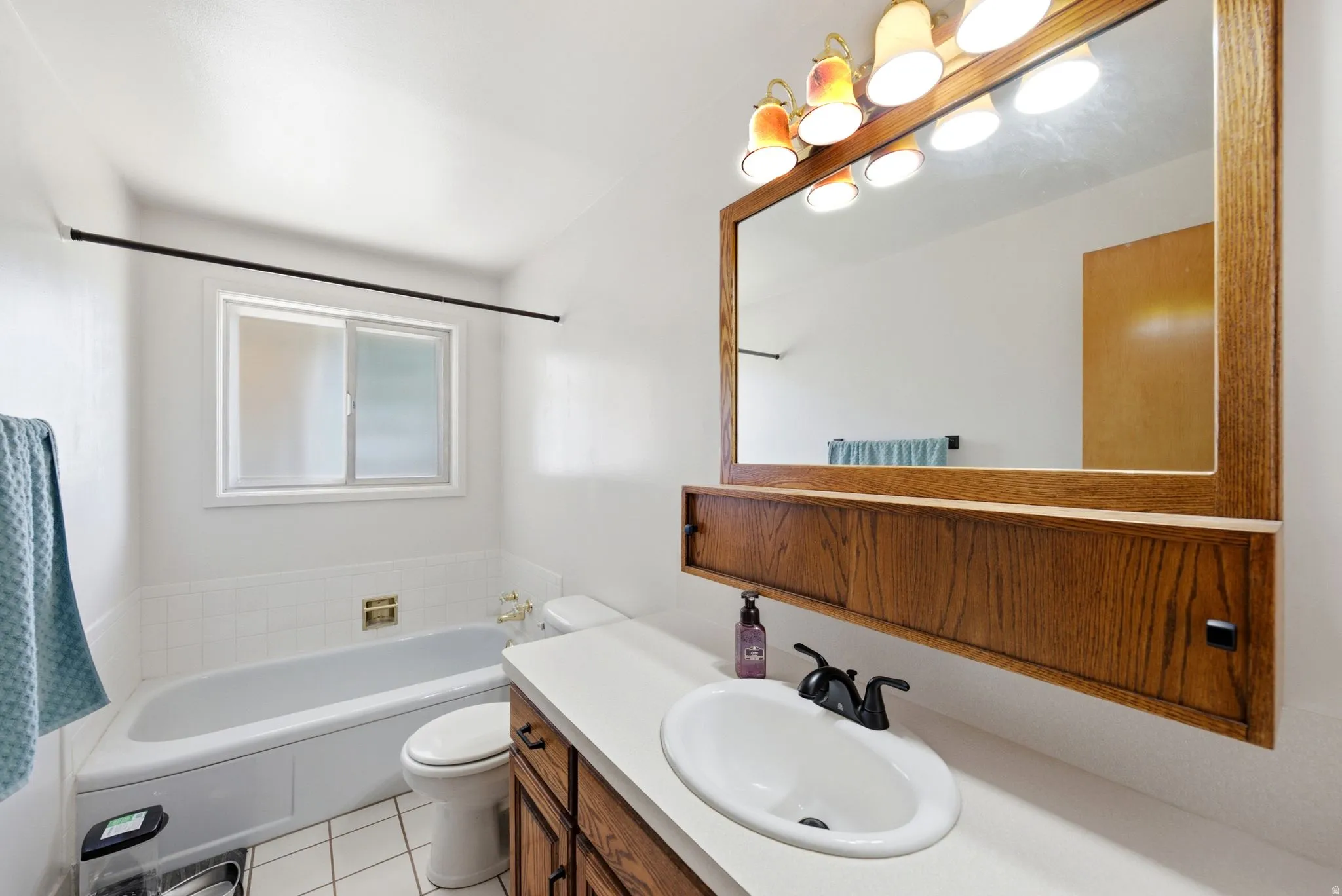 Bathroom featuring a white bathtub, a sliding window, and a wood-framed mirror with integrated lighting
