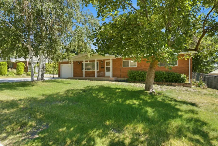 Brick exterior home featuring a covered front entry, an attached single-car garage, and a level front lawn with mature trees