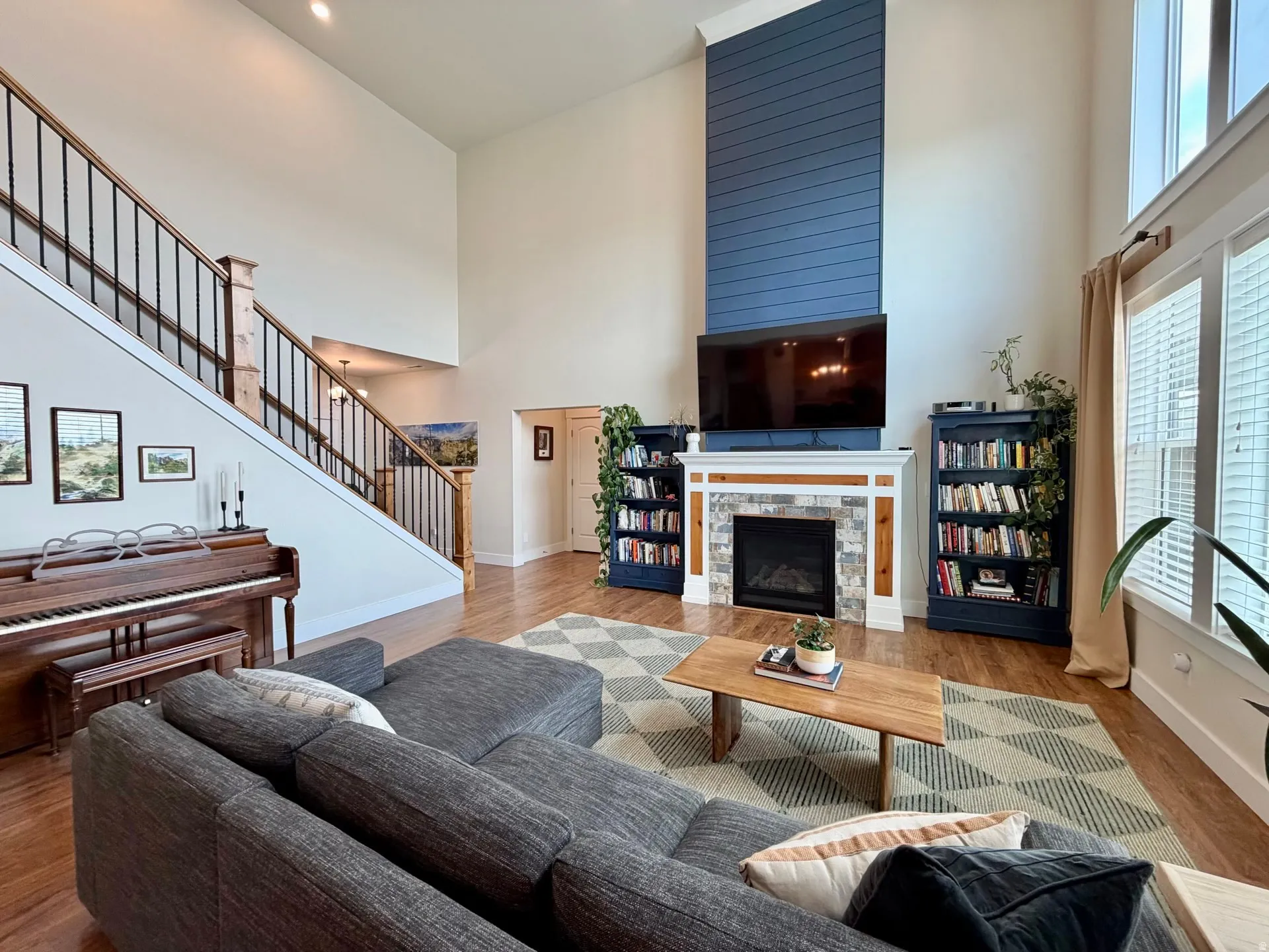 Two-story living area featuring a stone-surround fireplace with a shiplap accent wall, hardwood-finish flooring, a contemporary staircase with iron balusters, and expansive windows