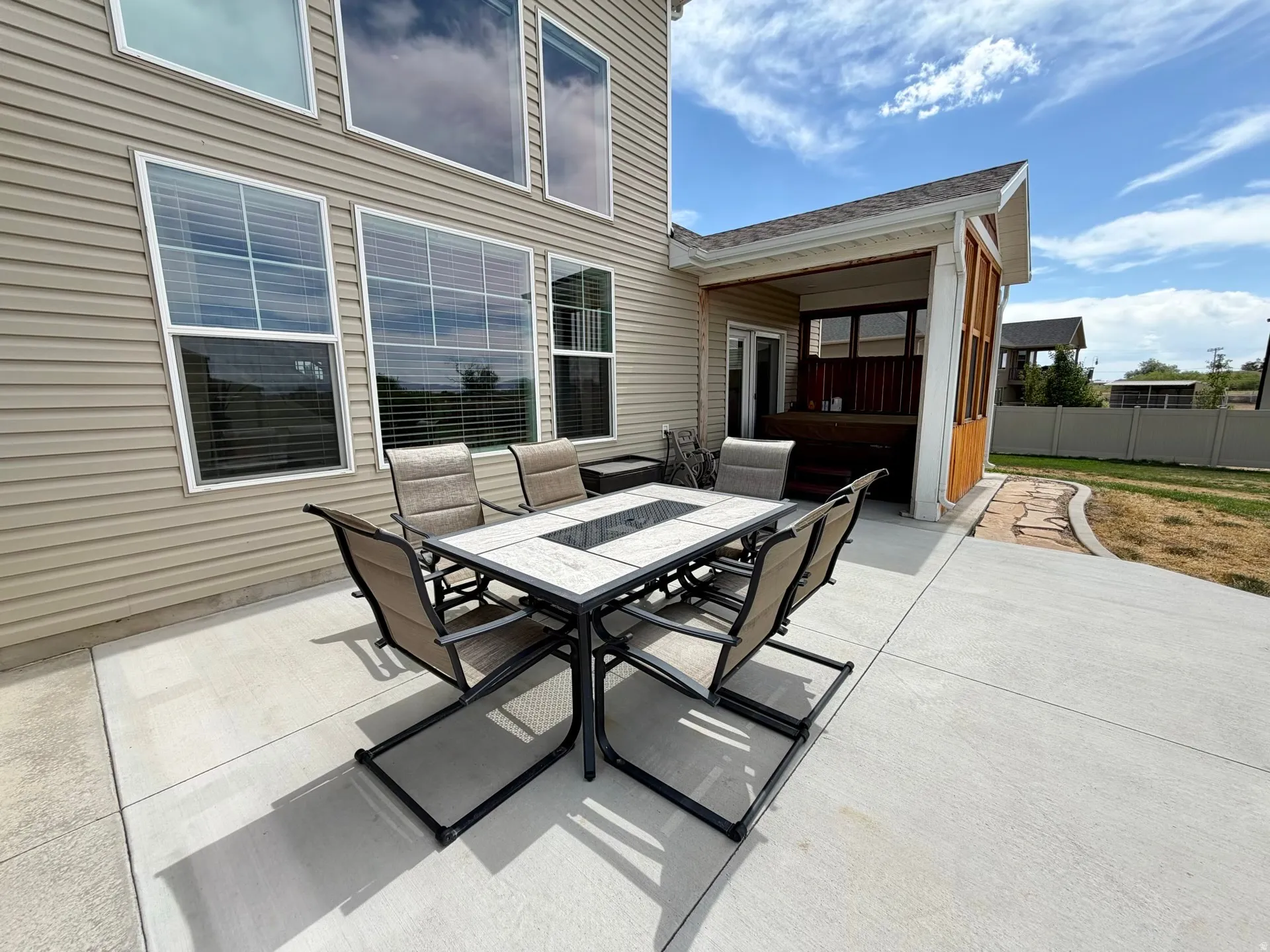 Spacious concrete patio with an adjacent covered deck, featuring siding exterior and multiple windows